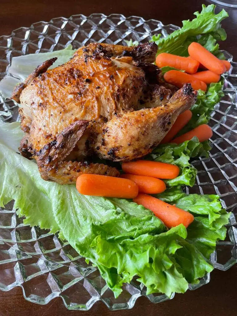 A perfectly cooked Cornish hen placed in a big plate with some orange carrots and green lettuce.