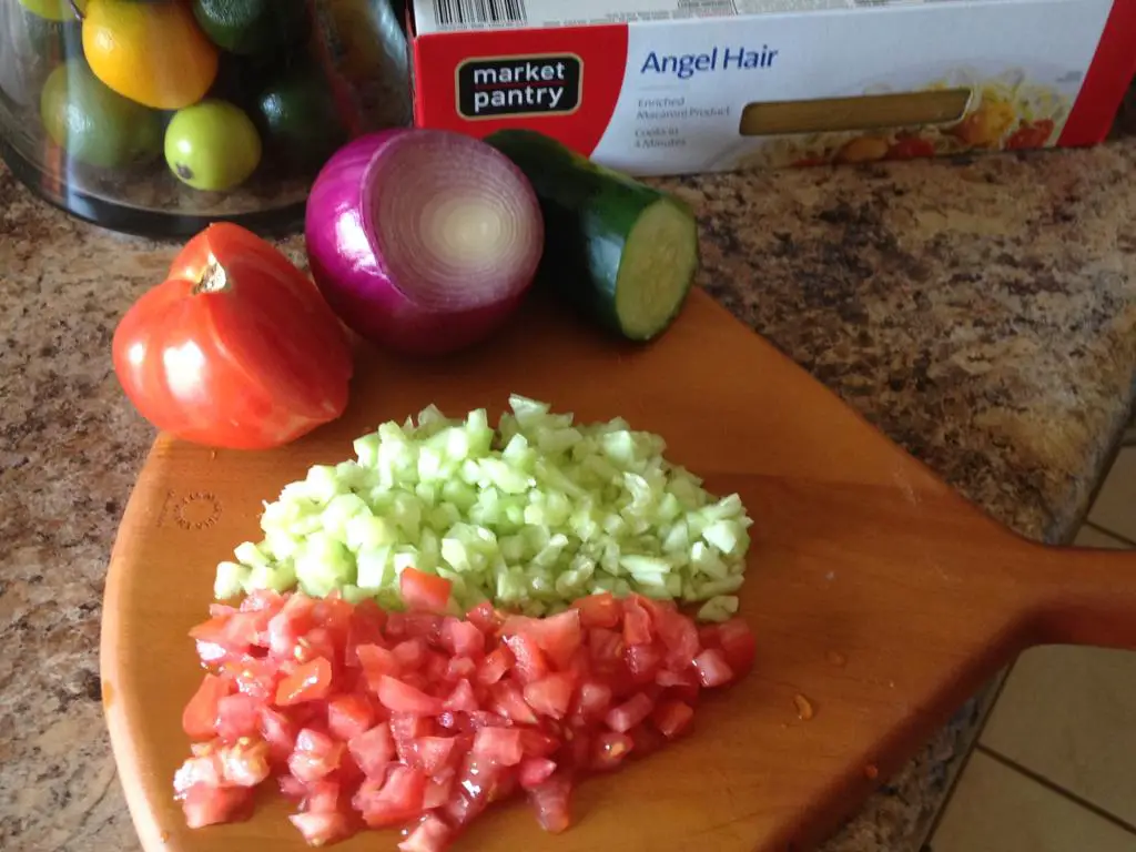 Diced tomato, cucumber, and red onion  on a board ready to be added to the summer pasta salad.