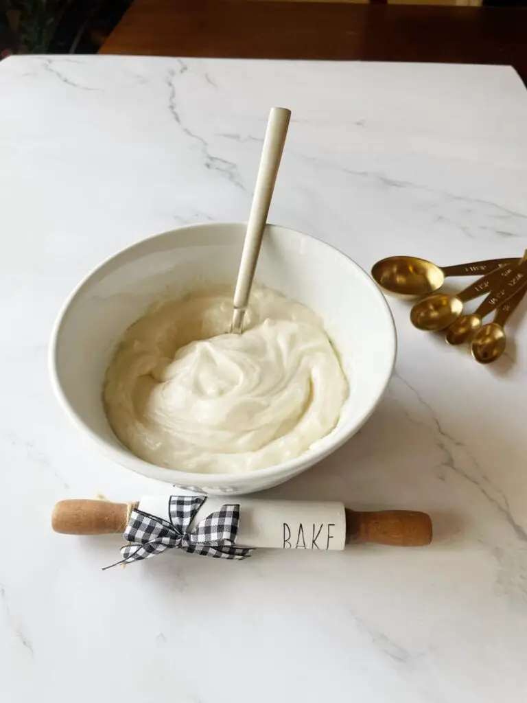 easy to make cream cheese icing in a white bowl surrounded by decorative cooking tools