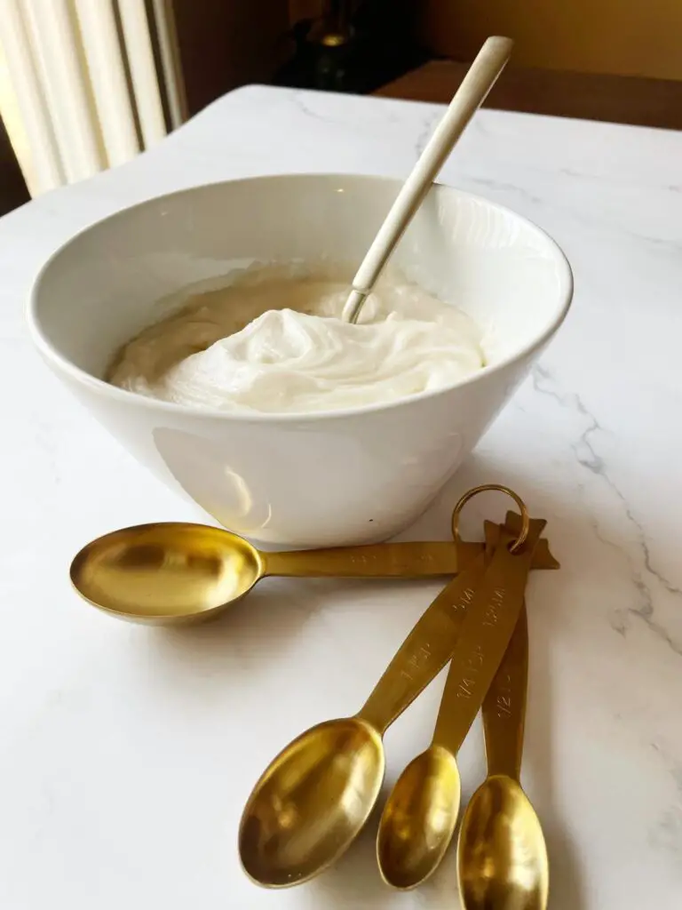 easy how to make cream cheese icing in a white bowl with gold measuring spoons next to it