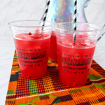 Homemade Juneteenth Red Punch served over ice in festive cups displayed on colorful African print fabric.