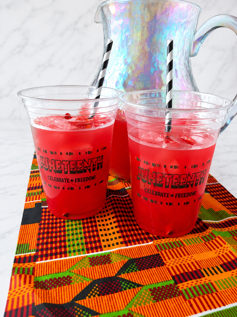 Homemade Juneteenth Red Punch served over ice in festive cups displayed on colorful African print fabric.