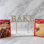 Betty Crocker German chocolate and lemon box cake mixes displayed beside a sparkling BAKE sign on a white marble background.